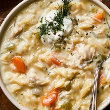 Creamy chicken orzo soup in a bowl, garnished with herbs and served with bread