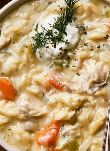 Creamy chicken orzo soup in a bowl, garnished with herbs and served with bread
